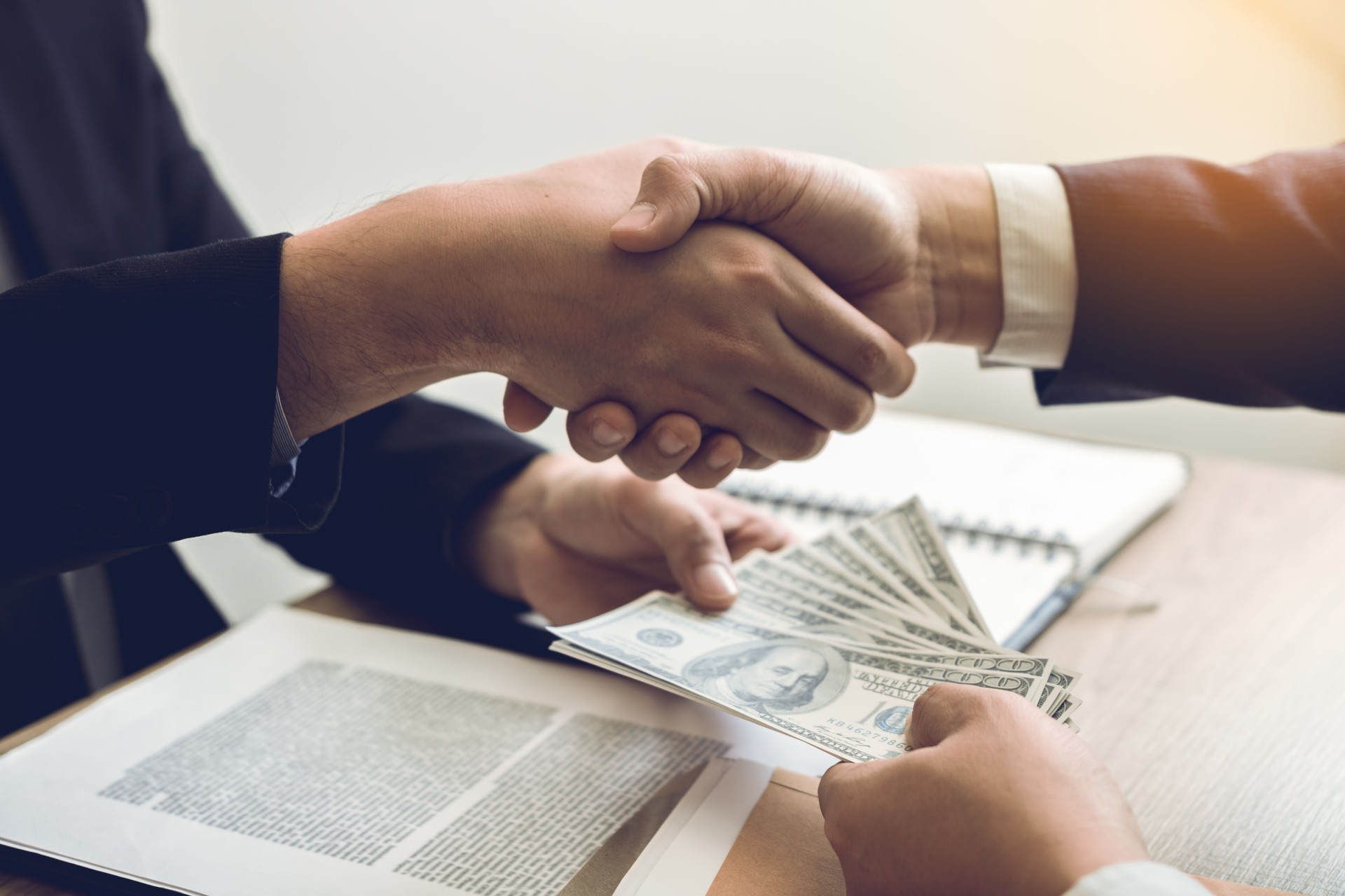 Two corporate businessmen shaking hands while one man giving money and receive cash dirty in office room with corruption concept.